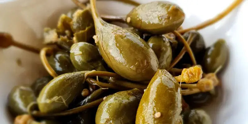 Kapern - Fleischige Knospen in einer weißen Schüssel, ideal für kulinarische Köstlichkeiten und Geschmackserlebnisse.