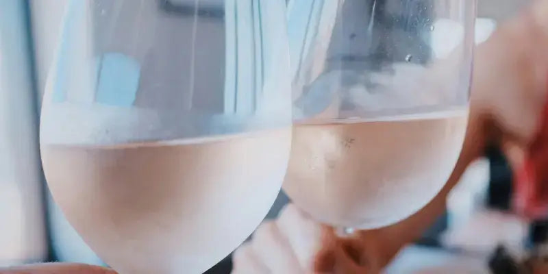 Roséwein: Zwei Gläser Roséwein anstoßen im Sommerlicht, farbenfrohes Ambiente.