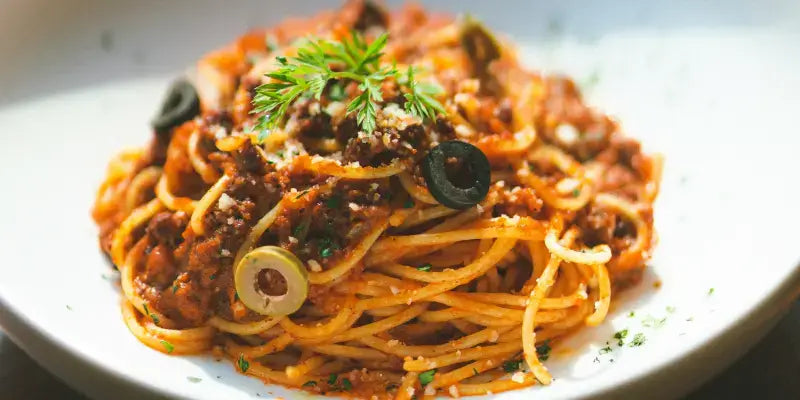 Pasta con Salsa di Capperi Fruttati auf einem Teller mit Oliven und frischer Petersilie garniert.