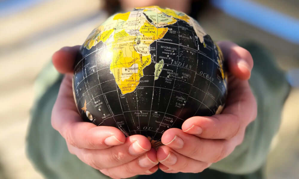 Liefert ihr ins Ausland? Person hält globus mit Afrika-Ansicht in den Händen, symbolisiert internationale Lieferung.