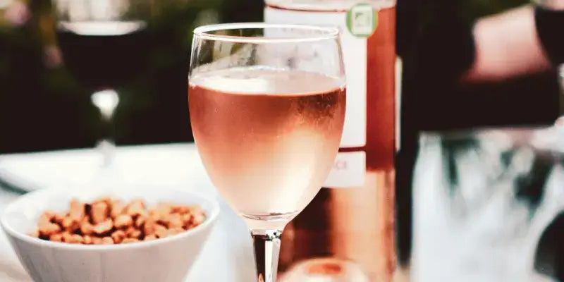Roséwein im Weinglas neben einem Snack, ideal zur Veranschaulichung der Roséweinproduktion.