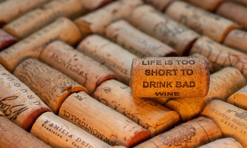 Weinflaschen-Korken mit dem Spruch „Life is too short to drink bad wine“ auf einer Ansammlung von Korken.