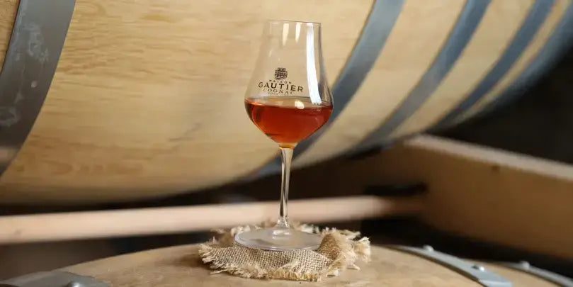 Maison Gautier Cognac in einem Glas vor Eichenfässern, die die Reifung des Edelbrands symbolisieren.