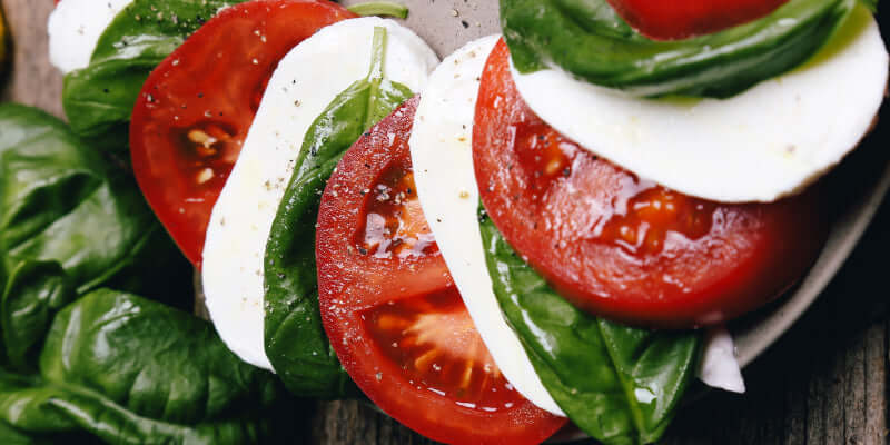 Tomaten Mozzarella und Spinat auf einem Teller, gewürzt mit Pfeffer und frischem Balsamico-Dressing.