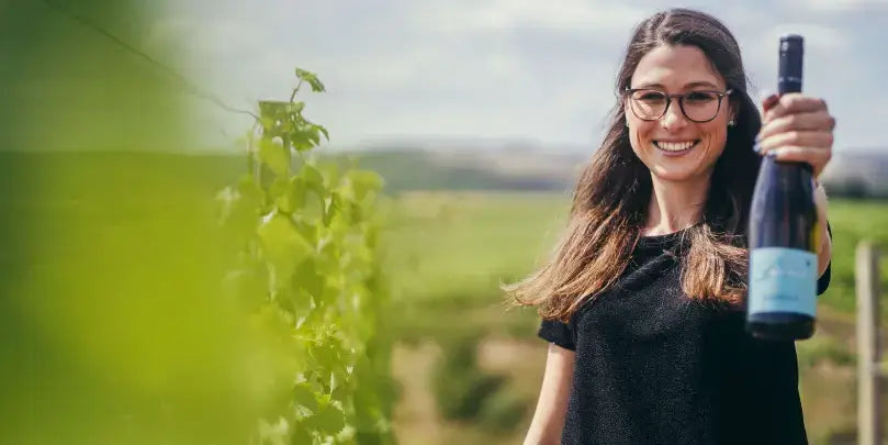 Weingut Udo Weber: Frau präsentiert Edition L Rosé im Weinberg, umgeben von grünen Reben.