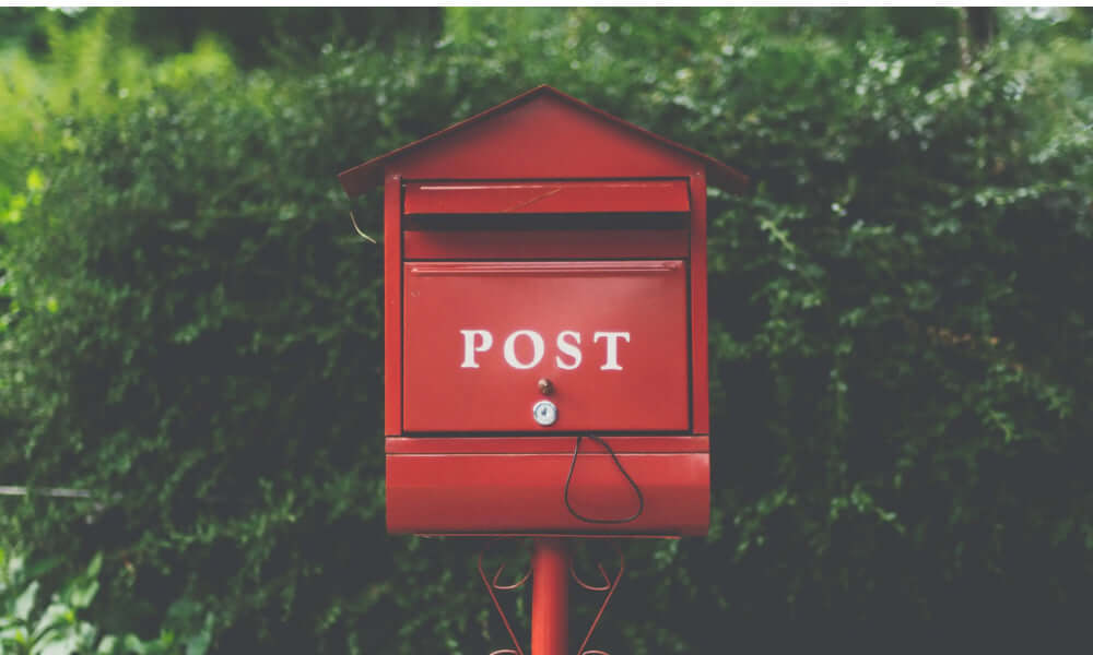 nostalgisch roter Briefkasten mit der Aufschrift Post vor einer Hecke