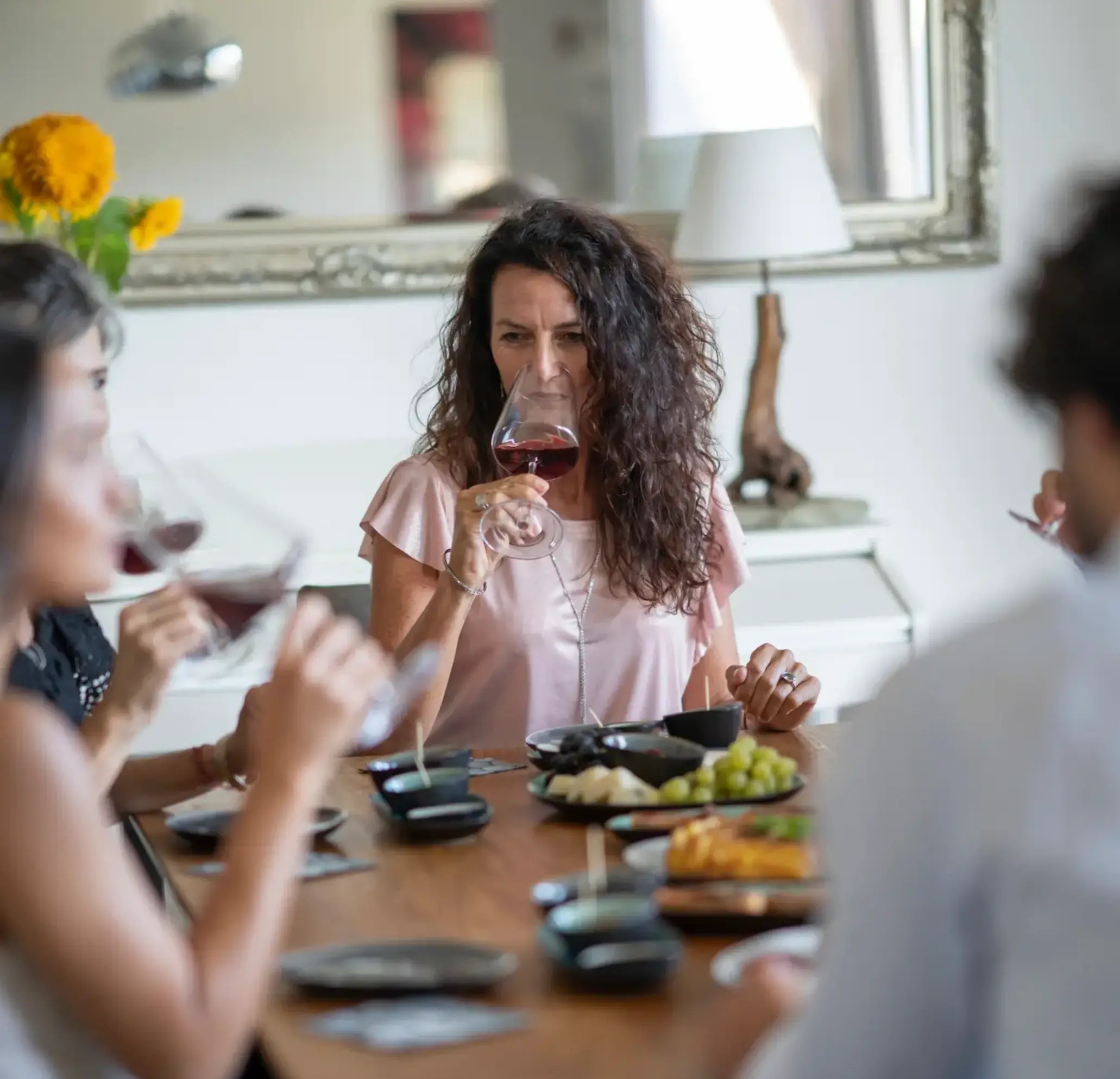 Mehrere Menschen sitzen am gedeckten Tisch und genießen ihr Wein Tasting. Drei Frauen riechen in ihr Glas mit Rotwein