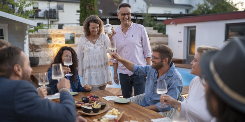Freunde beim Anstoßen auf der Terrasse, geselliges Beisammensein, entspannte Atmosphäre, TIME 2 TASTE.
