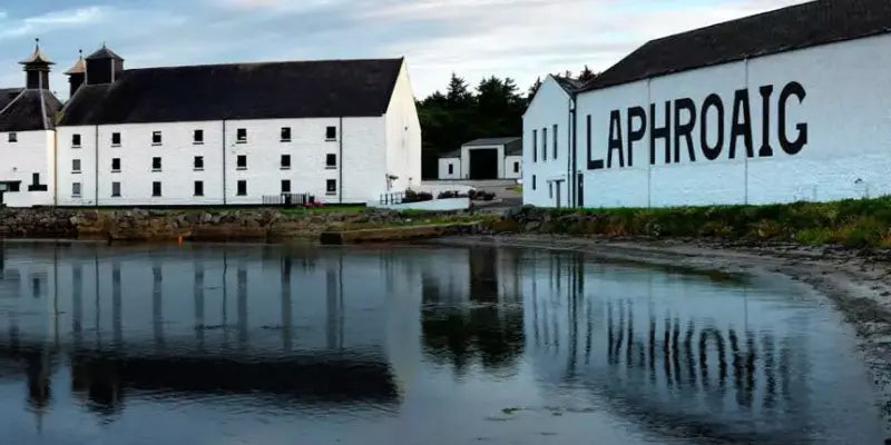 Laphroaig Brennerei in Islay, reflektiert im Wasser, bekannt für hochwertigen Whisky und traditionelle Herstellung.