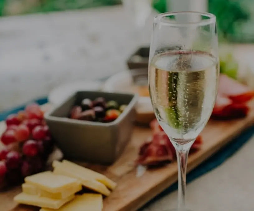 Sektglas mit Trauben und Käse auf einem Holzbrett, ideal für feste Anlässe und gesellige Zusammenkünfte.