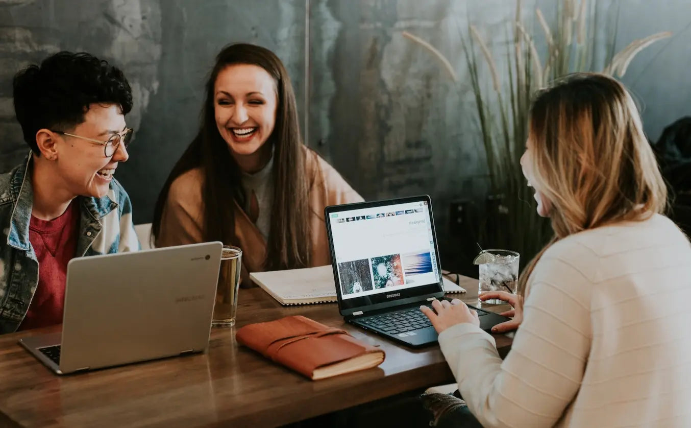 Zeit für Geschmack: Drei Personen arbeiten gemeinsam an Laptops in einem modernen Café und tauschen Ideen aus.