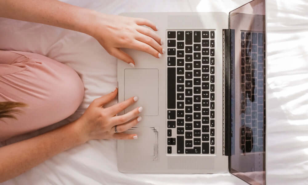 Produkt nachbestellen auf Laptop, Hände tippen auf der Tastatur, entspannte Atmosphäre im Schlafzimmer.