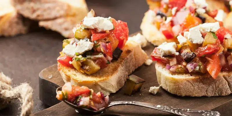 Oliven Bruschetta auf geröstetem Brot, garniert mit frischem Gemüse und Feta-Käse, ideale mediterrane Vorspeise.