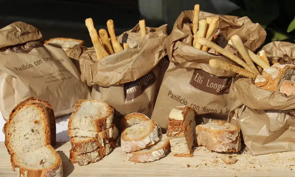 Auf einem Tisch liegen Brotscheiben, Grissini in Papiertüten