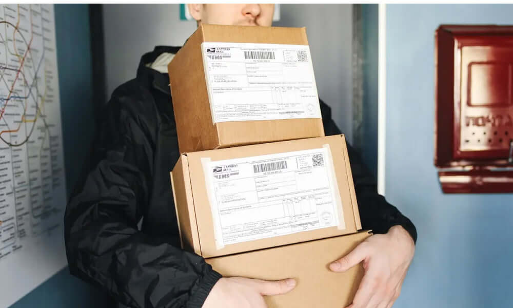 Mehrere Pakete werden von einer Person in einer Wohnung gehalten, die Versandetiketten zeigt.