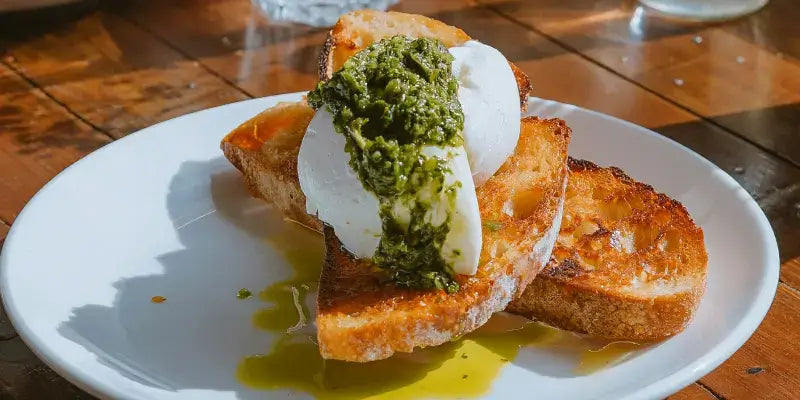 Rucola Pesto auf geröstetem Brot mit Mozzarella, angerichtet auf einem weißen Teller.