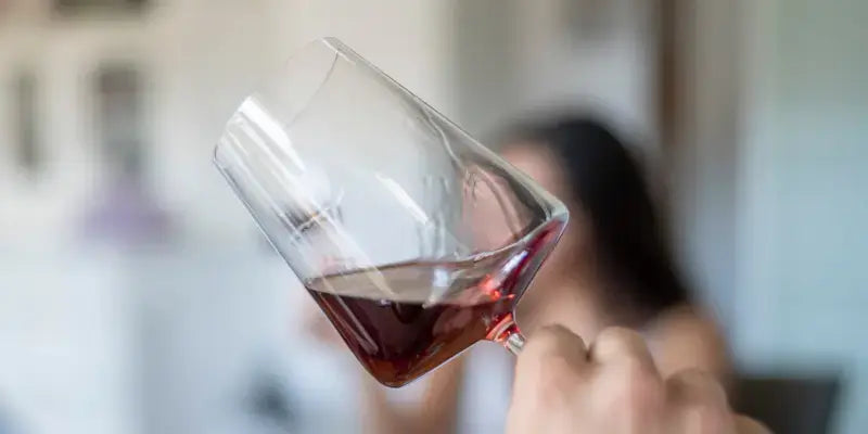Die Weinverkostung: Rotwein wird in einem Glas gehalten, während einer Person beim Probieren zugesehen wird.