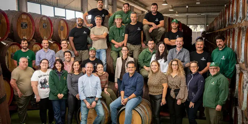 Justinos Madeira Teamfoto in der Produktionsstätte, umgeben von Weinfässern, in traditioneller Atmosphäre.