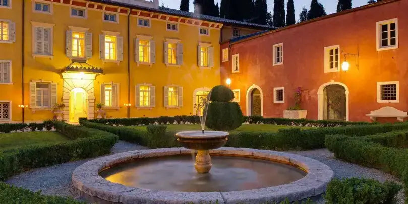 Amarone Della Valpolicella DOC Eduard: stilvolle Gartenanlage mit Brunnen und beleuchteten historischen Gebäuden bei Nacht.