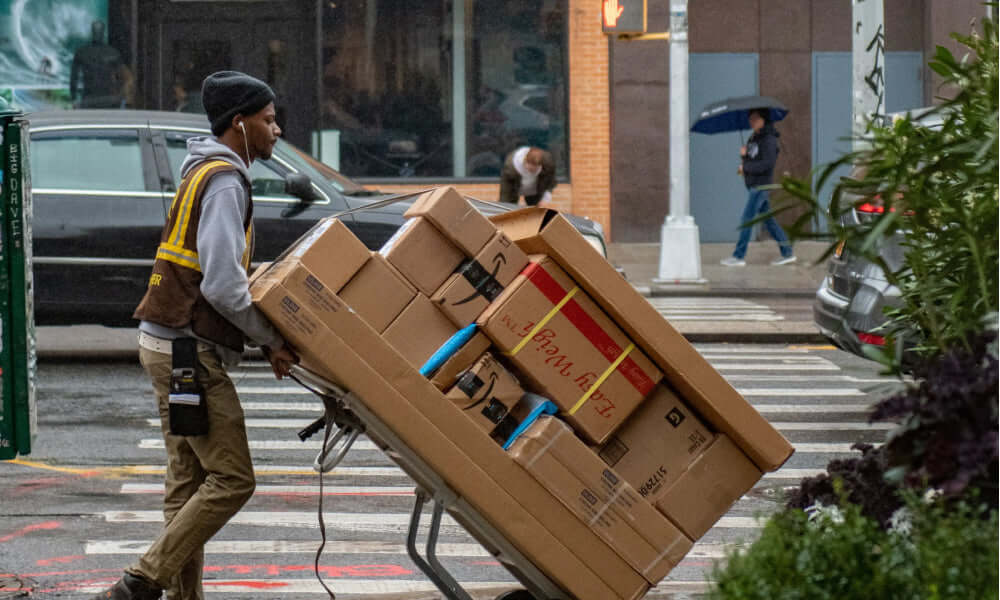 Schneller Versand: Zusteller transportiert Pakete auf einem Handwagen über die Straße in einem urbanen Umfeld.