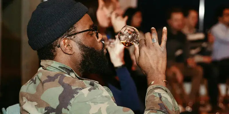 Rum: Mann genießt ein Glas Rum bei einer Verkostung, umgeben von anderen Teilnehmern.