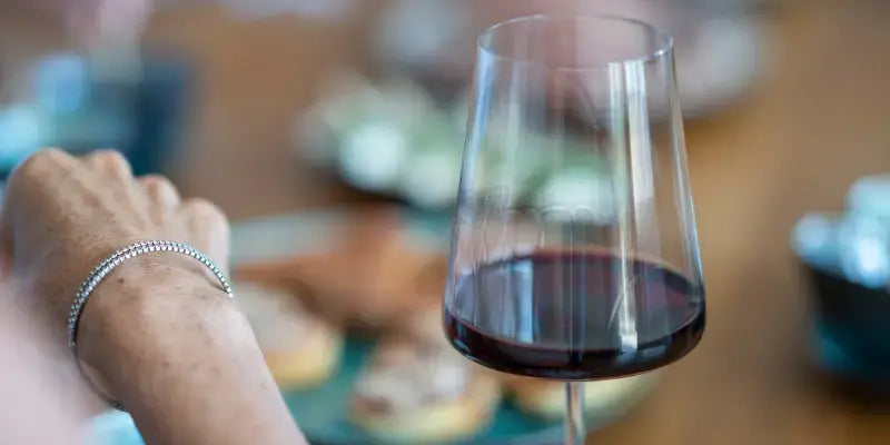 Kirchenfenster im Wein: Ein Glas Rotwein auf einem Tisch voller Snacks, entspannte Atmosphäre.