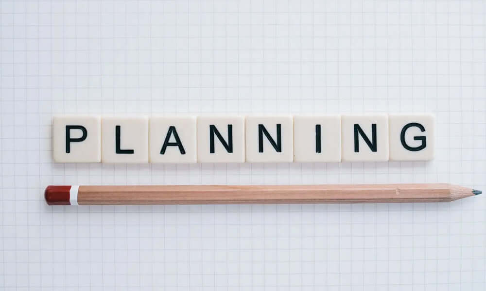 Planung mit Buchstaben auf Kachel und Bleistift auf kariertem Papier für strategische Projekte.
