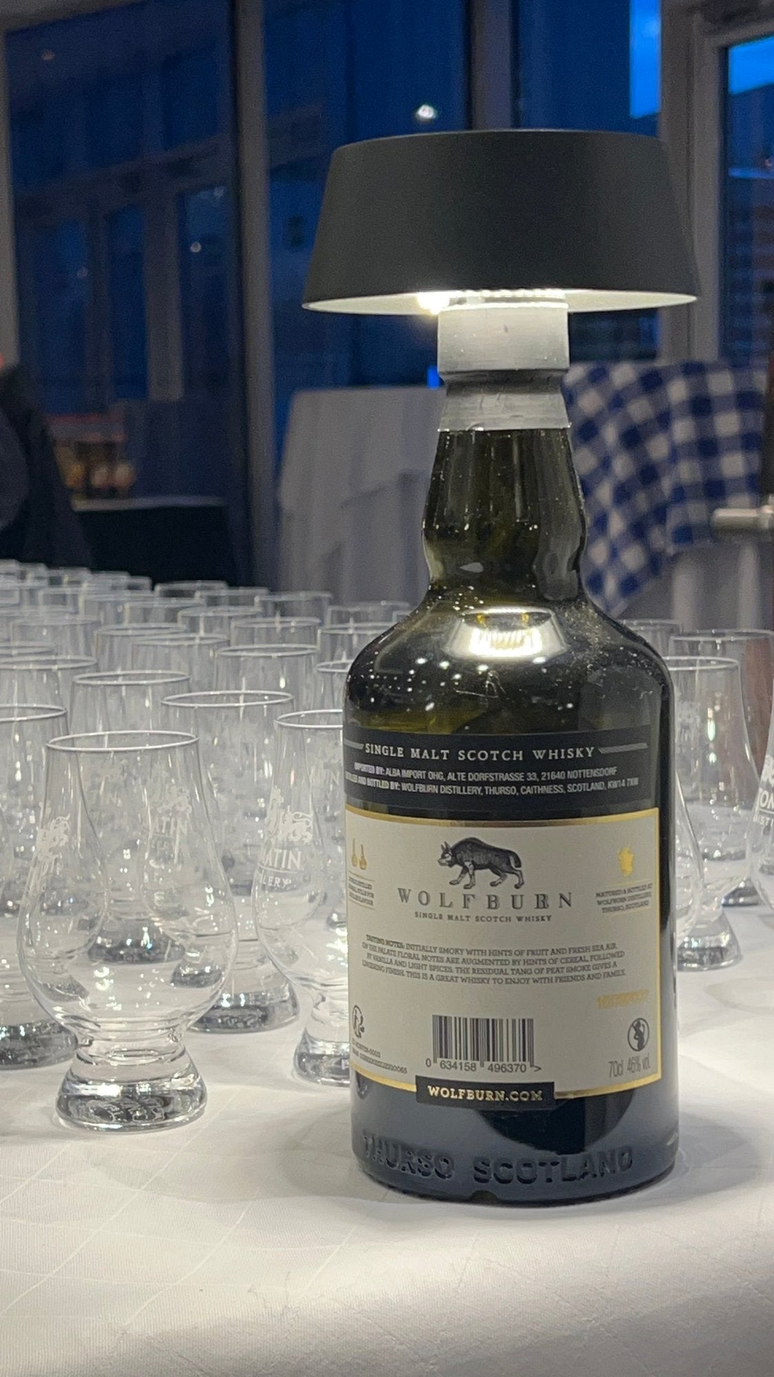 Whiskyflasche mit Leuchte vor vielen Tasting-Gläsern