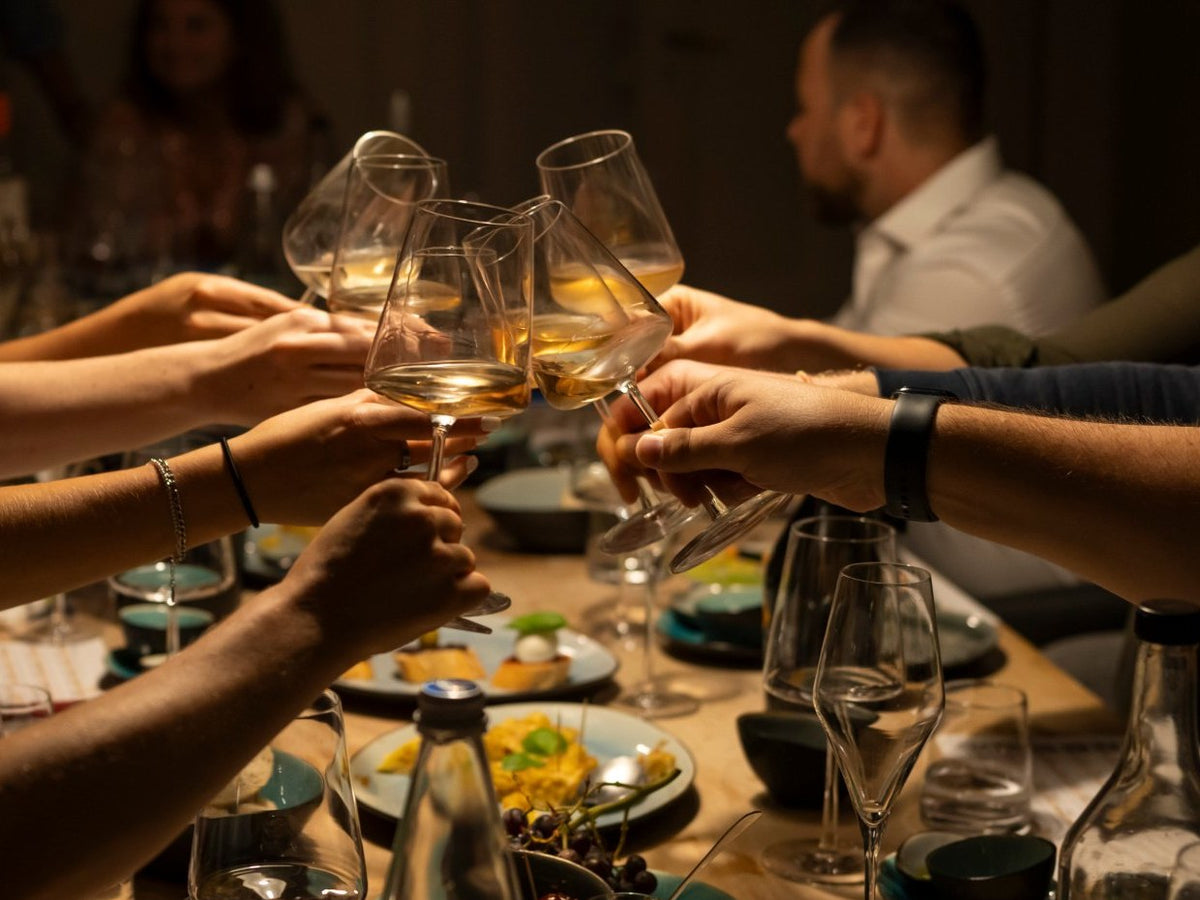 Gläser mit Weißwein beim Anstoßen, darunter Teller mit Fingerfood