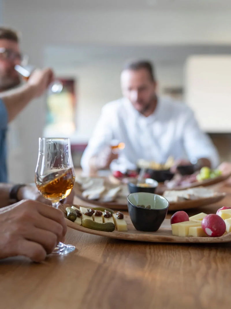 Gäste verkosten aus Nosing-Gläsern an einem Tisch mit Käseplatte