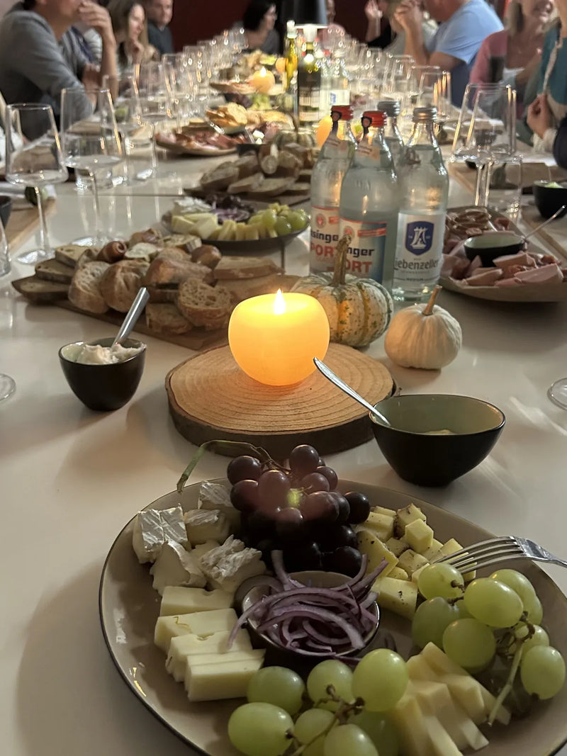 Gäste an einer langen Tafel mit Wein, Käse und Kerzen