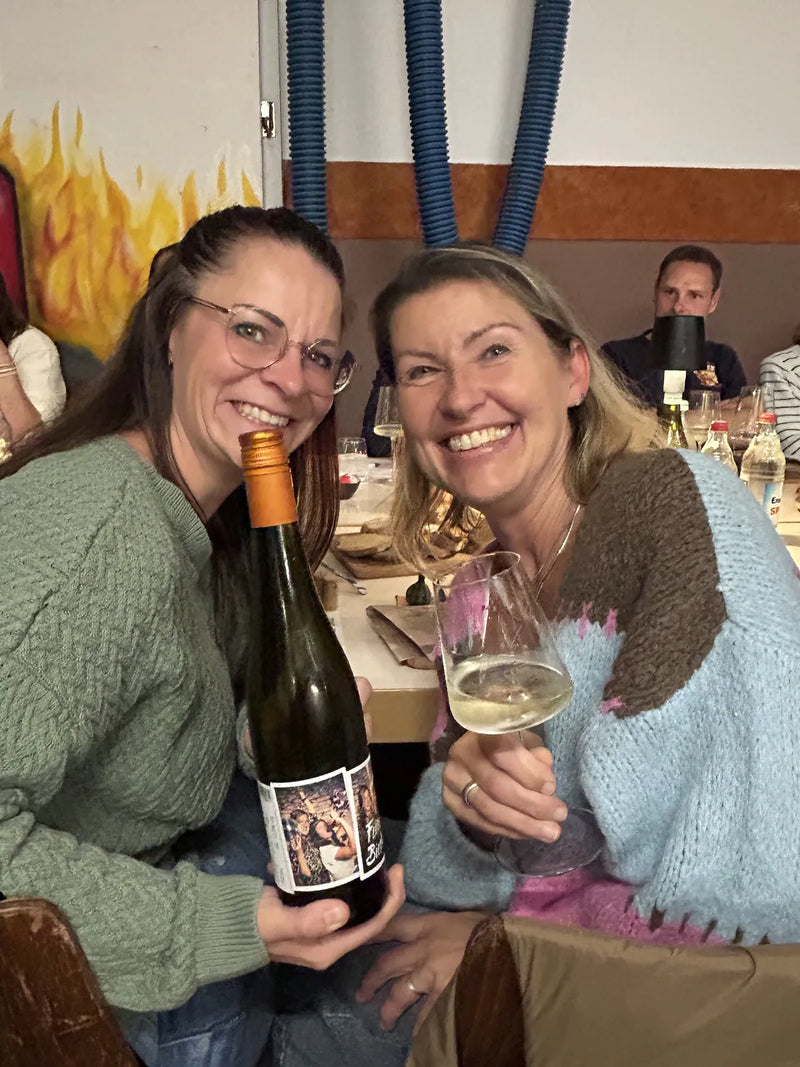 Zwei Gäste lachen mit einem Glas Weißwein bei der Weinprobe