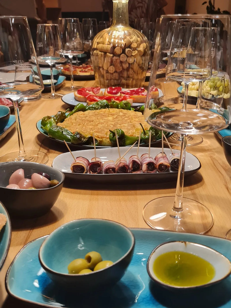 Tapas mit Tortilla, Pimientos und Oliven zwischen Weingläsern