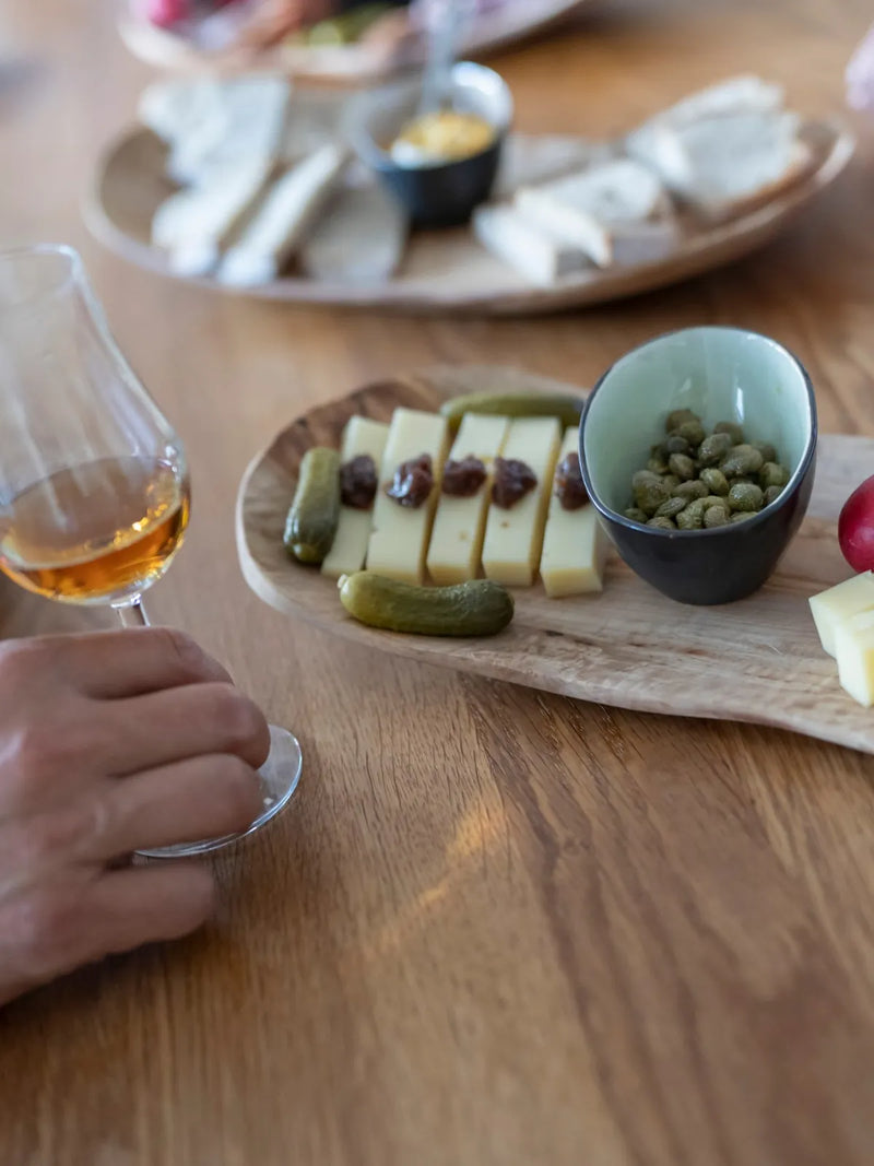 Nosing-Glas mit Whisky neben einer Platte mit Käse, Gürkchen und Radieschen