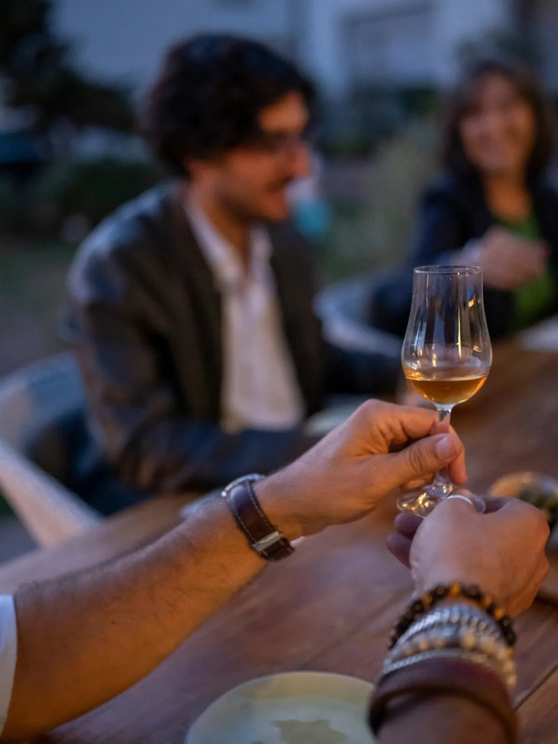 Ein Glas Whisky in der Hand, im Hintergrund weitere Gäste